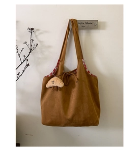 Détail d'un sac cabas en daim marron avec doublure à carreaux rouges et charme croissant