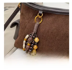 Detail of brown suede bag featuring colorful handcrafted beaded charm and gold hardware