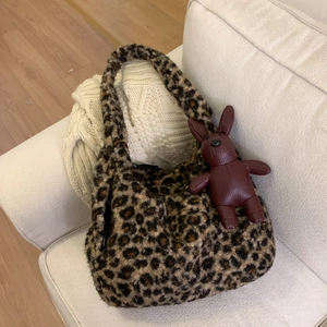 Close-up of leopard print plush tote bag with a red rabbit leather charm on a soft sofa