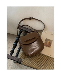 Close-up of a brown PU leather crossbody bag with bow detail on a woven chair