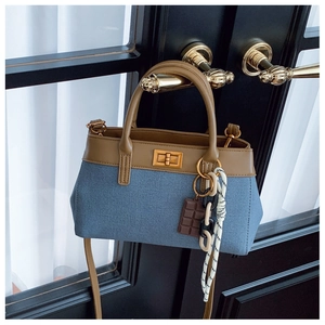 Detail of denim and brown leather bucket bag with gold lock and charm on a black door handle