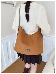 Side view of a large brown suede bucket bag worn with a white sweater in a home setting