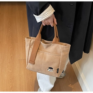 Détail du sac cabas en toile kaki avec broderie de dessin animé et poignée marron tissée