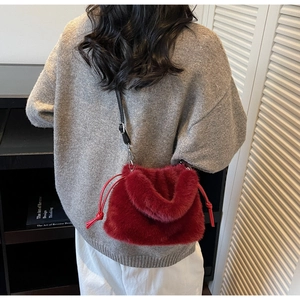 Détail d'un sac seau en fausse fourrure rouge avec bandoulière noire porté par un mannequin