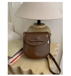Detail of a brown glossy leather crossbody bag with a bow and vintage aesthetic
