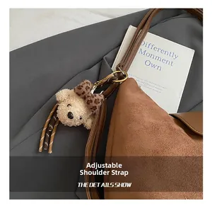 Close-up of brown suede shoulder bag with adjustable strap and cute bear charm