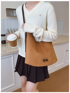 Brown suede half-moon tote bag with dark straps worn by a model in a minimalist setting