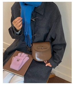 Close-up of vintage brown saddle bag with a leather bow detail on a stylish wool coat