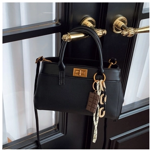 Detail of black textured handbag with golden rotary lock and decorative chocolate pendant