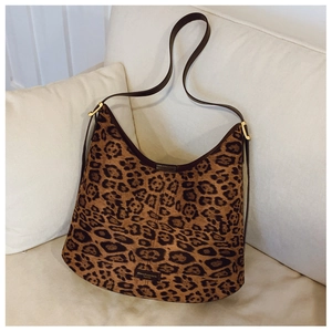 Close-up of leopard print bucket bag with leather strap and fashion logo on beige sofa