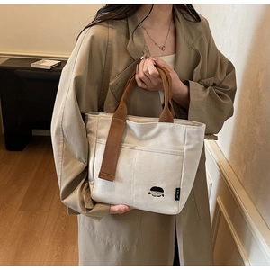 Détail d'un sac cabas en toile crème avec anses marron et broderie de dessin animé