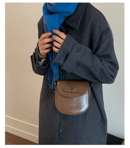 Brown semi-circular crossbody bag with bow detail worn over a stylish grey autumn wool coat