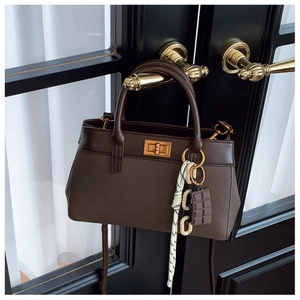 Detailed view of dark brown faux leather handbag with gold twist lock and woven charm