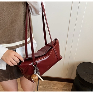 Detail view of burgundy patent leather shoulder bag with baseball charm on a model