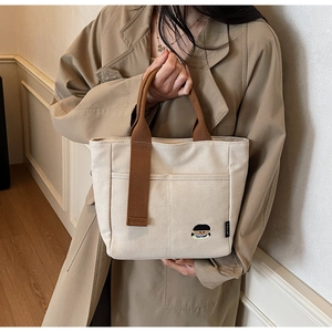 Détail du sac fourre-tout en toile crème avec anses brunes et broderie de dessin animé