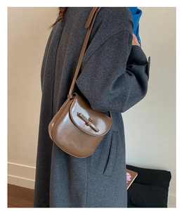 Glossy brown crossbody saddle bag shown from side back view on a dark grey wool coat