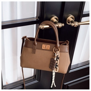 Detail of canvas bucket bag with leather trim, gold twist lock and charm on a black door