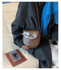 Close-up of brown vintage saddle bag with leather knot detail on a grey wool coat