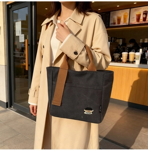 Détail du sac cabas en toile noire avec anses brunes et écusson brodé de dessin animé