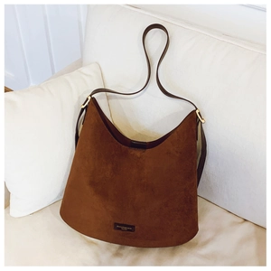 Detail of brown suede hobo bag with gold hardware and logo plaque on white sofa