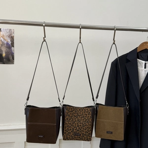 Trois sacs seaux en daim marron foncé, imprimé léopard et kaki suspendus sur un cintre