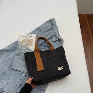 Détail du sac cabas en toile noire avec des anses tressées marron et une petite broderie cartoon
