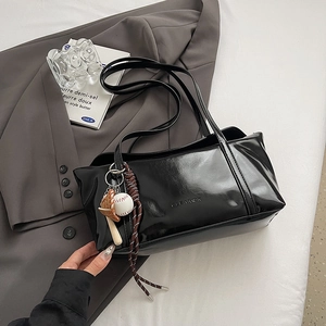 Detail shot of black glossy underarm bag with baseball charms and woven rope decoration