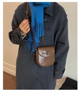 Brown vintage leather saddle bag with flap buckle shown on dark coat and blue scarf