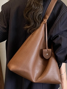 Brown lychee leather tote bag with wide shoulder strap worn over a pinstripe blazer