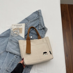 Gros plan détaillé du sac cabas en toile beige avec broderie cartoon et anses marron