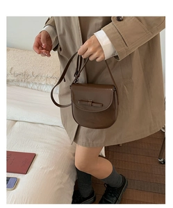 Detail of dark brown crossbody bag with bow accent worn over a khaki trench coat