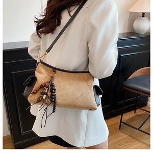 Detail of khaki suede shoulder bag with retro wooden bead tassel and gold hardware