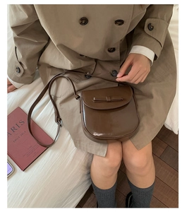 Detail of vintage brown leather crossbody bag with bow accent on a khaki coat