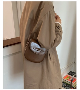 Detail of a vintage dark brown glossy saddle bag with unique knot strap on a beige trench coat