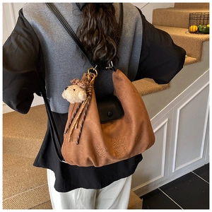 Close-up of brown suede crescent bag with sheep plush charm and embossed pattern