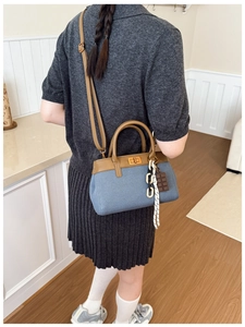 Detail of gray canvas bucket bag with brown leather handle and chocolate charm