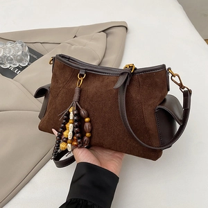 Detailed view of dark brown suede handbag with decorative wooden bead tassels and leather trim
