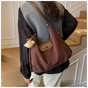 Detail of dark brown hobo bag with embossed cartoon design and plush bear charm decoration