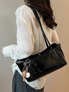 Glossy black underarm tote bag with logo embossing and baseball pendant on shoulder