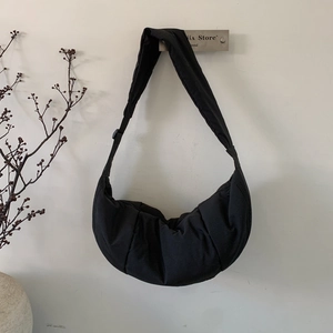 Detail of black crescent crossbody bag with pleated texture and wide adjustable strap