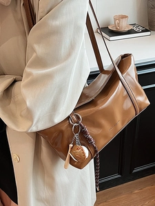 Brown glossy underarm bag with baseball charm and Cle Arson logo over a beige trench coat