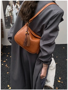 Détail d'un sac à bandoulière caramel avec glands et perles en bois sur une veste de costume