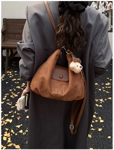 Brown suede hobo bag with cartoon embroidery and teddy charm shown on autumn street