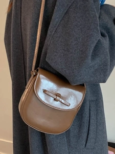 Vintage brown glossy leather crossbody bag with bow-shaped flap shown on a wool coat