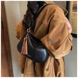 Détail d'un sac à bandoulière noir brillant avec pompon et perles en bois sur mannequin