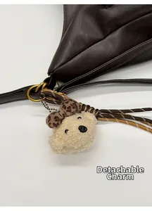 Close-up of detachable beige plush bear charm with leopard bow on brown tote bag
