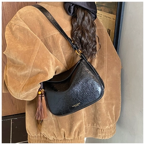 Détail d'un sac à bandoulière noir brillant avec pompon porté sur une veste en daim
