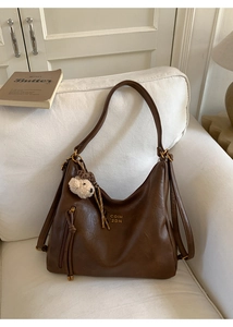 Detail of dark brown leather tote bag with logo branding and cute teddy bear charm