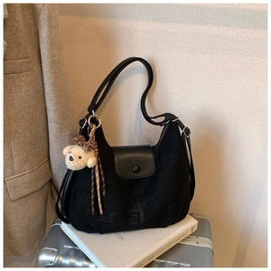 Detail of black suede shoulder bag with bear pendant and cake embroidery on a suitcase