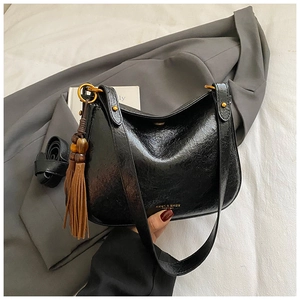 Détail du sac à bandoulière noir brillant avec garniture dorée et pendentif à glands